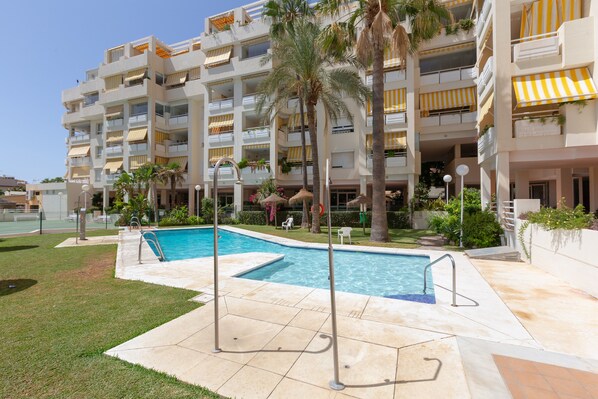 Un hôtel doté d’une piscine, de palmiers et de balcons surmontés d’auvents jaunes.
