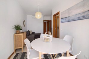 A dining area with a round table, white chairs, a basket, a wooden cabinet, and a painting on the wall.