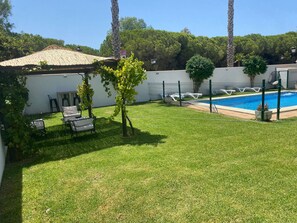 Un patio trasero con piscina, sillas de descanso, una pérgola y una pared blanca.