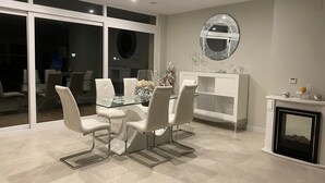 Un coin repas avec une table en verre, des chaises blanches, un buffet blanc et une cheminée.