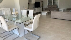 Un salon moderne avec une table à manger en verre, des chaises blanches, un canapé et un téléviseur.