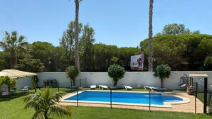 Un jardin à l’arrière de la maison, avec une piscine, entouré d’une clôture, et comprenant quelques chaises longues et un petit espace aménagé en jardin.