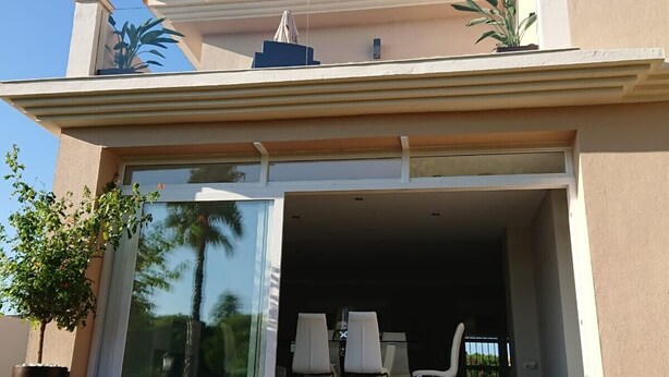 Une maison moderne dotée d’une grande porte vitrée, d’une terrasse avec des chaises et une petite table.