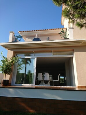 Une maison moderne dotée d’une grande porte vitrée, d’une terrasse avec des chaises et une petite table.