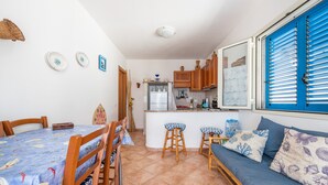 A kitchen with wooden cabinets, a refrigerator, and a dining area with a table and chairs. - Holiday Home Casa Vacanze 21 Aprile - T with Sea View & Terraces (Calasetta)