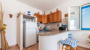 A kitchen with wooden cabinets, a white refrigerator, a granite countertop, and a blue checkered stool. - Holiday Home Casa Vacanze 21 Aprile - T with Sea View & Terraces (Calasetta)