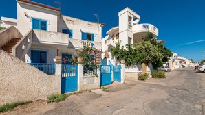 A residential street with white buildings, blue shutters, and a gated entrance. - Holiday Home Casa Vacanze 21 Aprile - T with Sea View & Terraces (Calasetta)