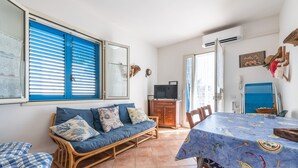 A room with a blue sofa, dining table, and a television. - Holiday Home Casa Vacanze 21 Aprile - T with Sea View & Terraces (Calasetta)