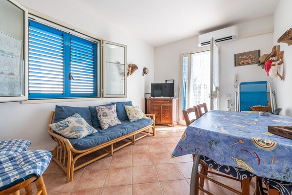 A room with a blue sofa, dining table, and a television.