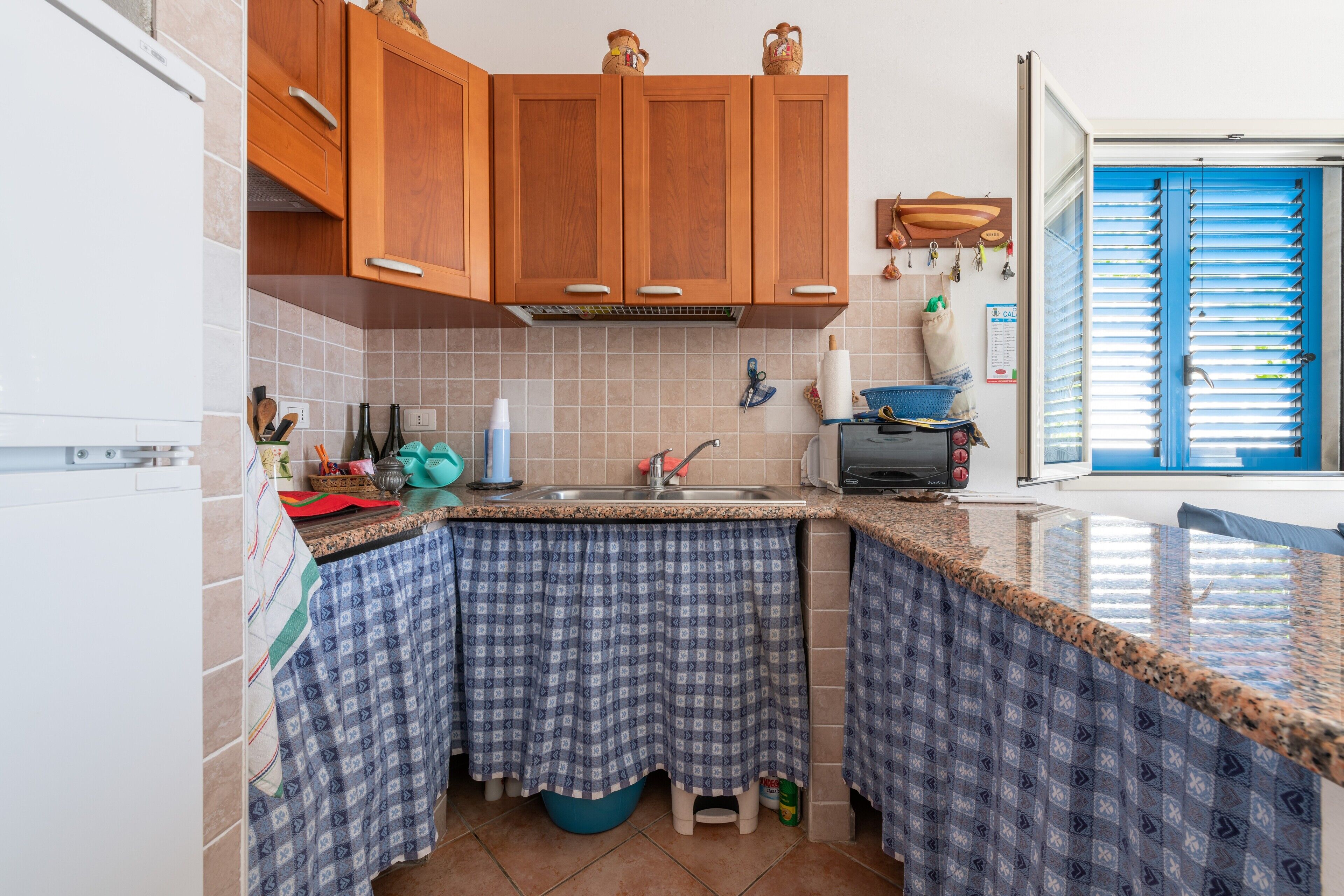 A kitchen with wooden cabinets, a sink, and a window with blinds.