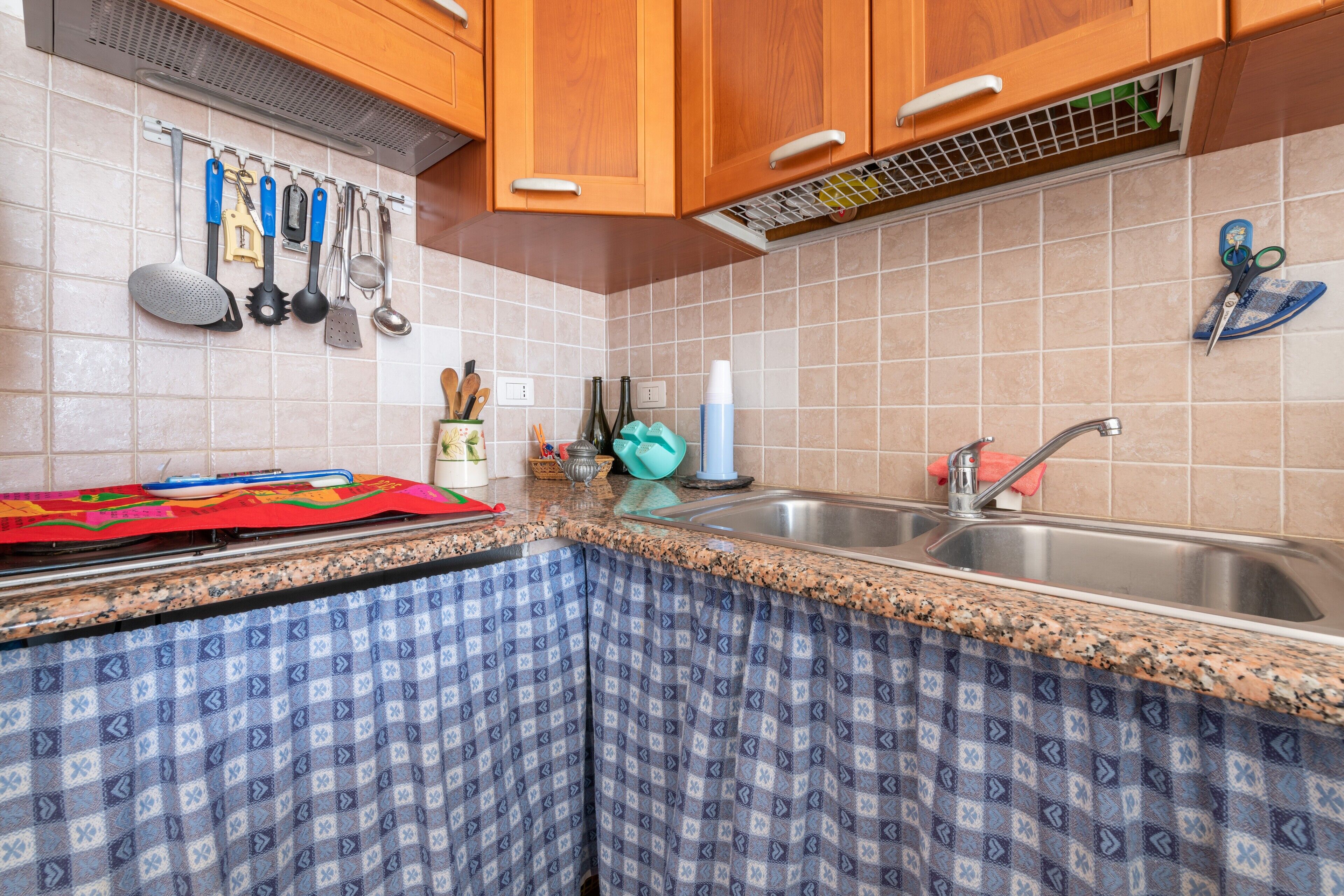 A kitchen with wooden cabinets, a granite countertop, a sink, and various utensils hanging on the wall.