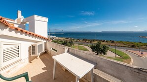 Ein Balkon mit weißem Tisch, Blick auf das Meer und eine kurvenreiche Straße.
