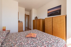 A bedroom with a patterned bedspread, a single pillow, a wooden wardrobe, and a wall-mounted picture.