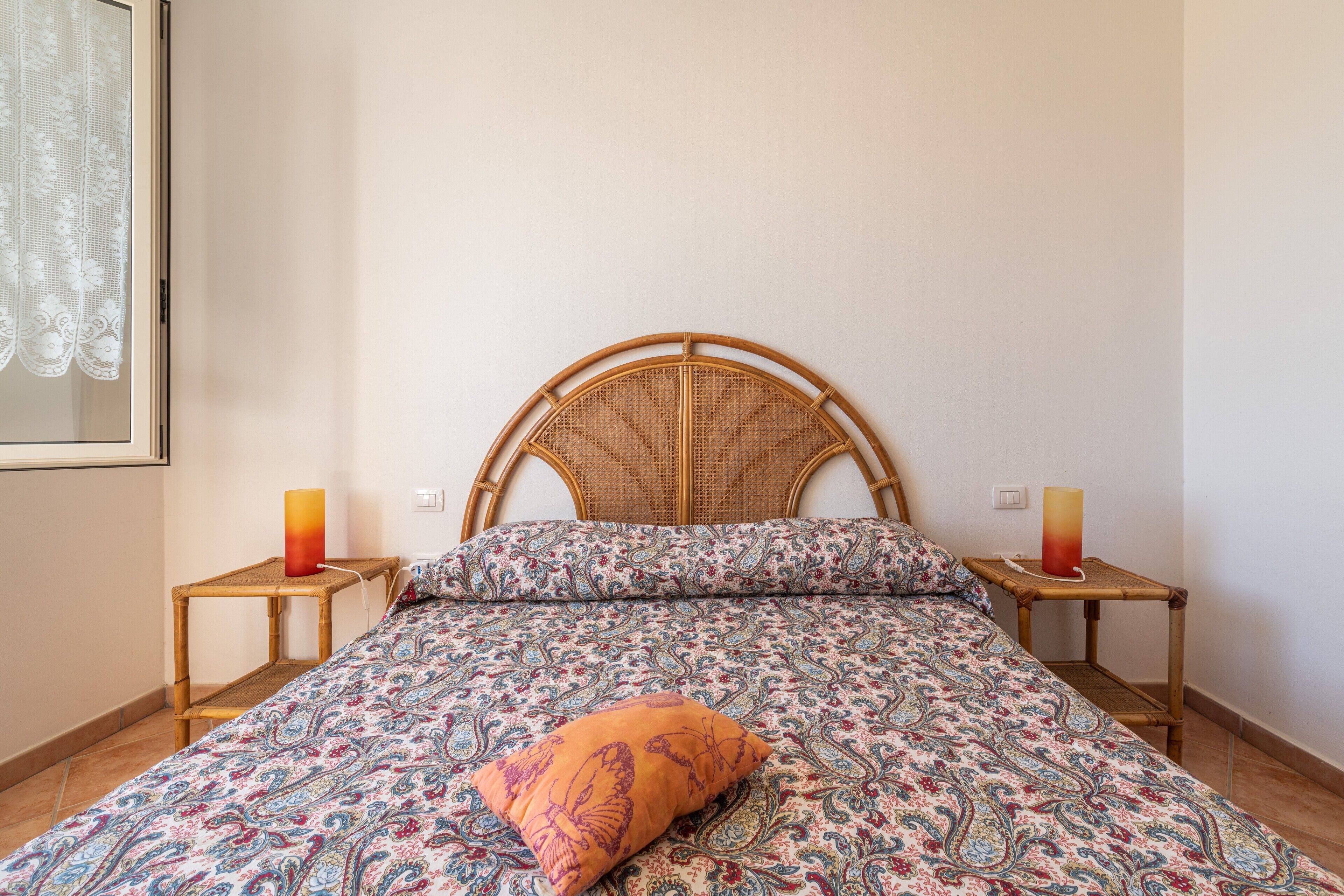 Un lit avec une couvre-lit à motifs, une tête de lit en bois, deux tables de chevet avec des bougies et un interrupteur fixé au mur.