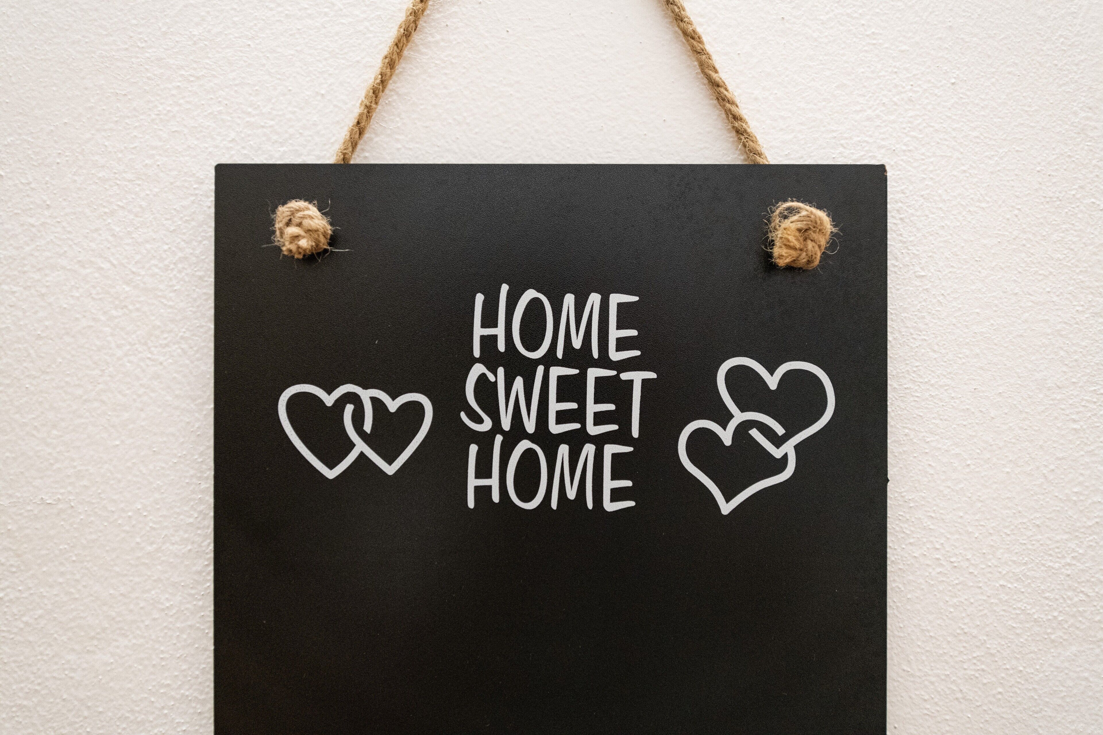 Une plaque noire sur laquelle on peut lire « HOME SWEET HOME » et qui est ornée de symboles en forme de cœur, et qui est accrochée à un mur blanc.