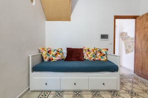 A bed with colorful pillows, a wooden door, and a patterned floor.