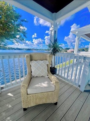 A wicker chair with a cushion on a wooden deck overlooking a body of water. - A Taste of Paradise @tnzwaterside (St. Petersburg)