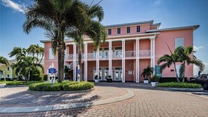 Un edificio rosa con una entrada central, rodeado de palmeras y una zona pavimentada.