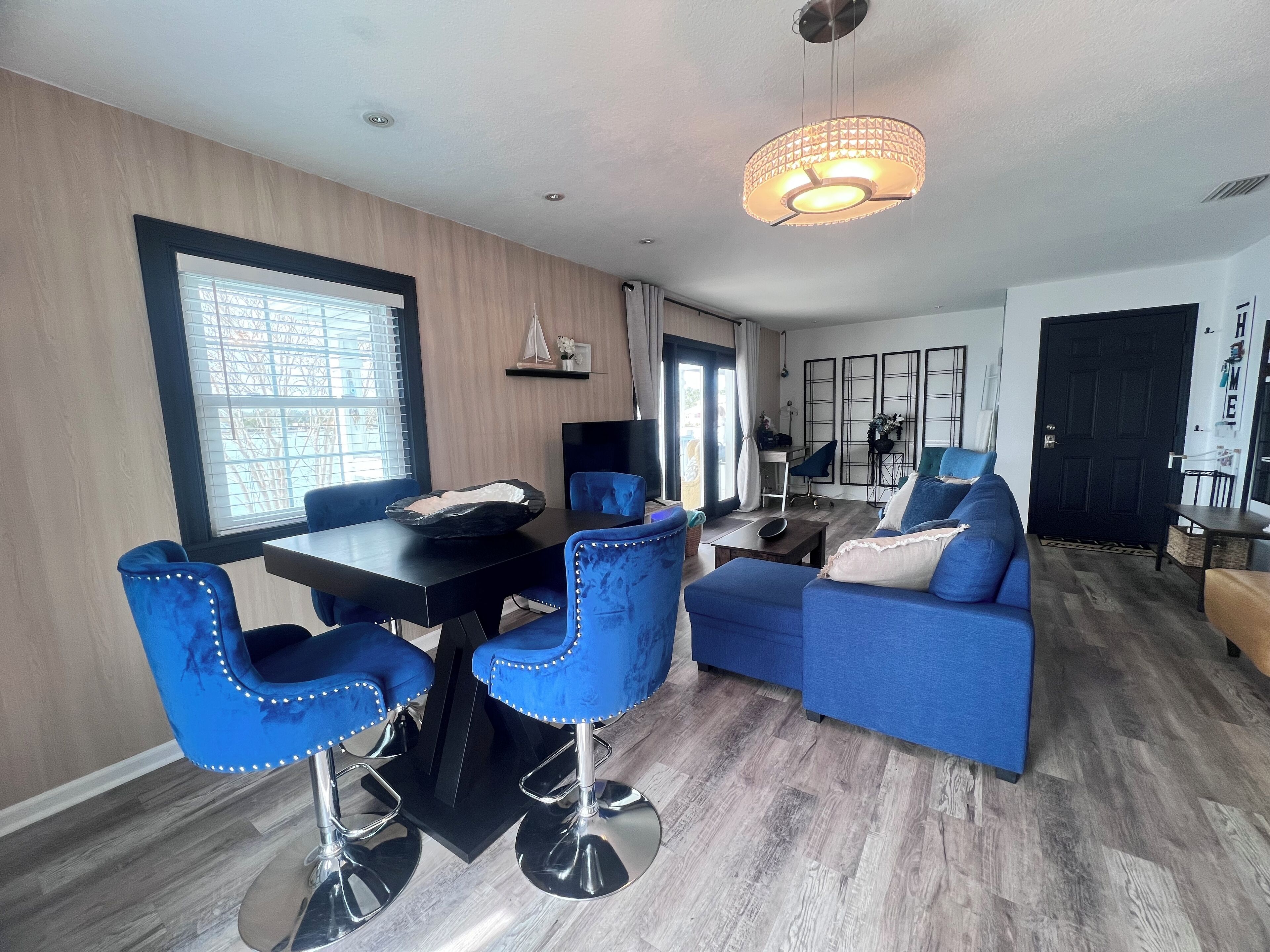 Ein modernes Wohnzimmer mit Essbereich, ausgestattet mit blauen Polsterstühlen, einem schwarzen Esstisch und einem blauen Sofa.