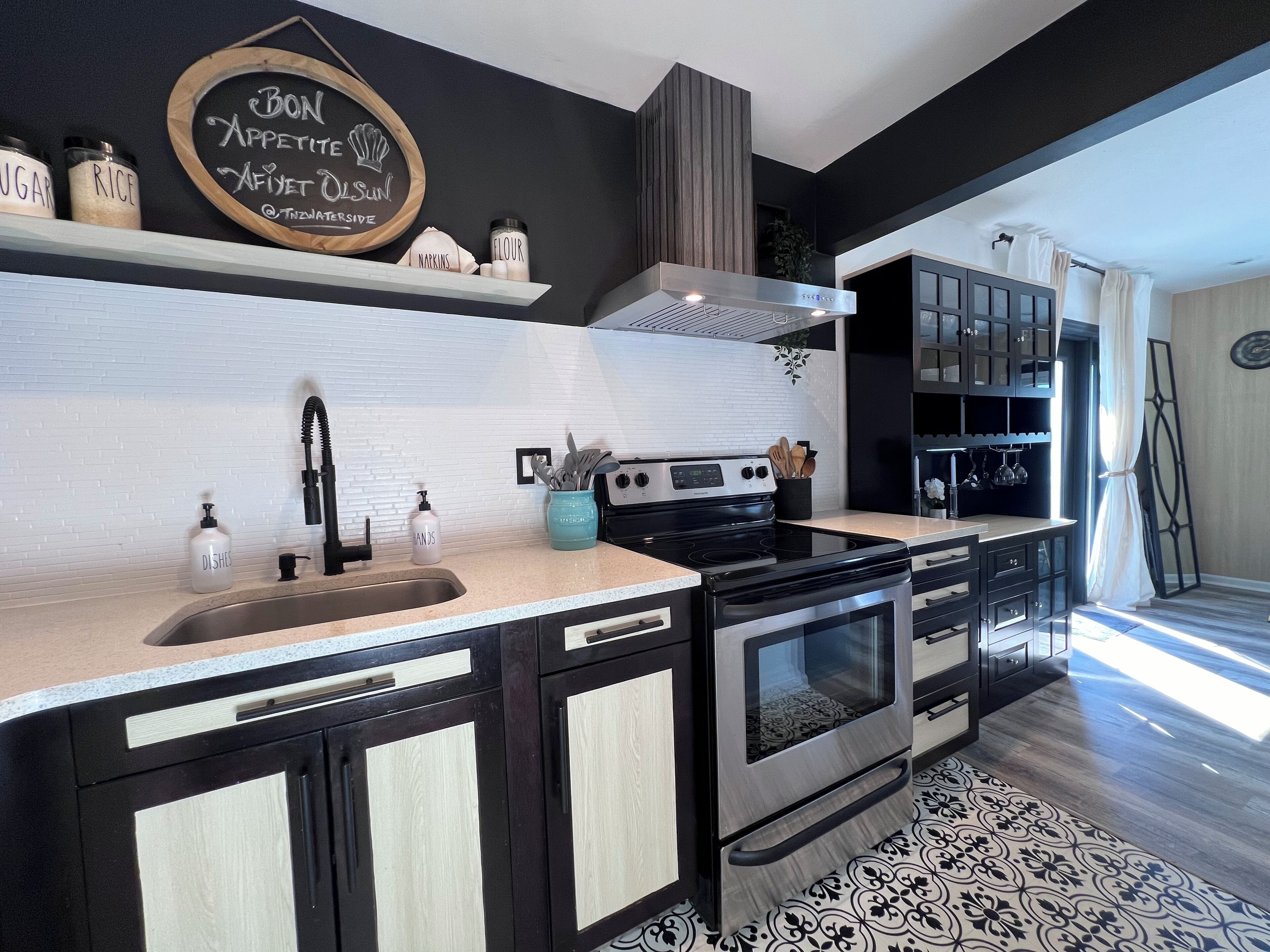 A modern kitchen with black cabinets, a stainless steel stove, and a chalkboard sign.