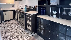 Una cocina moderna con gabinetes negros, piso con estampado blanco y negro y una campana extractora de acero inoxidable.