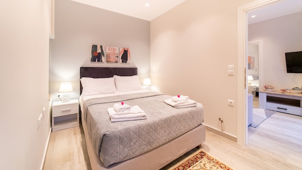 Ein Schlafzimmer mit Bett, Nachttischen, einem Fernseher und einer Tür zu einem weiteren Raum.