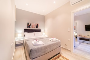 A bedroom with a bed, nightstands, a TV, and a door leading to another room.