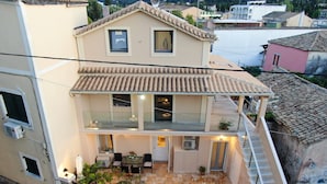Ein zweistöckiges Gebäude mit Balkon, Außenbestuhlung und einer terrasse aus Steinplatten.