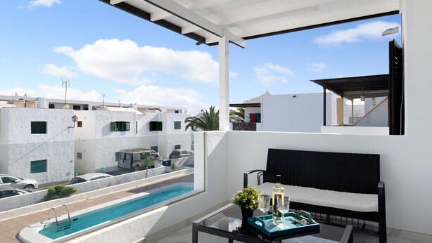 Ein Balkon mit Pool, einem Tisch, einer Flasche und Gläsern sowie einem schwarzen Stuhl.