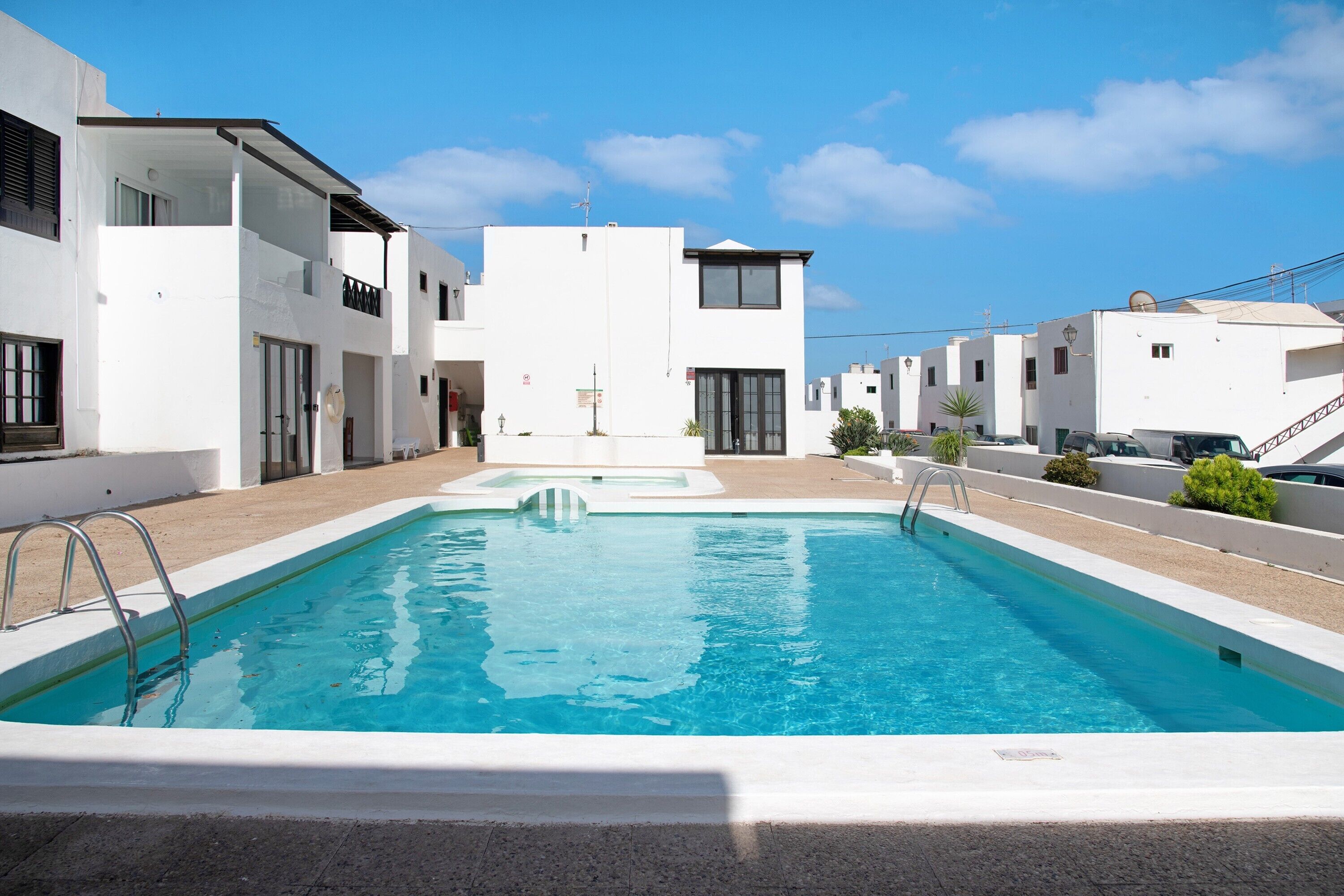 A modern pool area with a clear blue pool, white buildings, and a clear sky.