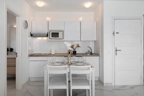 Une cuisine moderne avec des meubles blancs, un four à micro-ondes, un évier et une table à manger pour deux personnes.