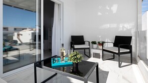 Ein Balkon mit Glastisch, zwei Korbstühlen, einem Topfpflanzen und einer Flasche.
