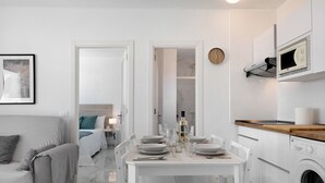 Eine moderne Küche mit Einbauwaschmaschine, ein Essbereich mit Tisch für vier Personen und ein Schlafzimmer mit Bett und Nachttisch.