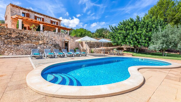 Piscina con pared de piedra, sillas de descanso y un edificio de piedra con tejado de baldosas.