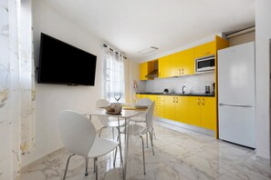 Una cocina moderna con armarios amarillos, un refrigerador blanco y un televisor de pantalla plana montado en la pared.