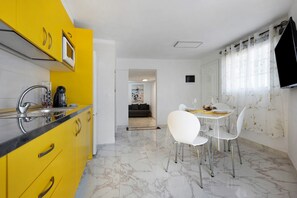 A modern kitchen with yellow cabinets, a dining area with white chairs, and a marble floor.