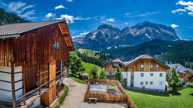 Eine Holzhütte mit geneigtem Dach, umgeben von einem Holzzaun, mit Blick auf Berge im Hintergrund.