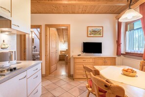 A kitchen with wooden cabinets, a dining table with a bowl of fruit, and a television on a stand. - Apartment Ciasa Raut App Valüz with Mountain View, Garden & Wi-Fi (La Val)