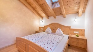 Ein Schlafzimmer mit Holzboden, Oberlicht, einem Bett mit floralem Bettzeug, Nachttischen und einem Nachtschränkchen.