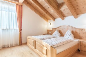 A wooden bed with a headboard, a bedside table, a lamp, and a window with curtains.