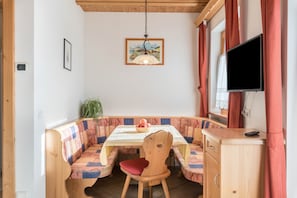 A dining area with a table, benches, a chair, a television, and a plant.
