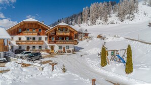A wooden chalet with balconies, a snow-covered driveway, and a ski slope in the background. - Apartment Ciasa Raut App Santa Berbura with Mountain View, Balcony & Wi-Fi (La Val)