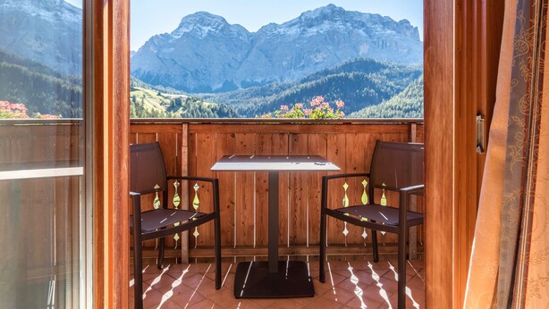 A balcony with a wooden table and two chairs, overlooking a mountainous landscape. - Apartment Ciasa Raut App Santa Berbura with Mountain View, Balcony & Wi-Fi (La Val)