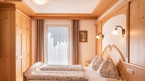 A wooden-framed room with a bed, a nightstand, a mirror, and a window with curtains. - Apartment Ciasa Raut App Santa Berbura with Mountain View, Balcony & Wi-Fi (La Val)
