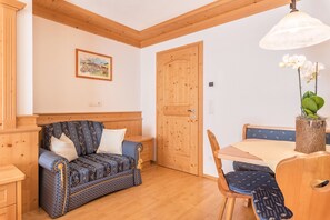 Une pièce avec un plafond en bois, une porte en bois, un canapé, une table à manger avec des chaises et un luminaire suspendu.