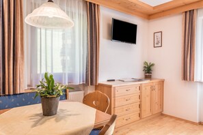 A room with a wooden dining table, a potted plant, a television mounted on the wall, and a cabinet with drawers.