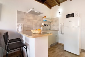 Una cocina con un refrigerador blanco, un microondas, una tetera y un lavamanos. Hay dos sillas negras y una encimera de madera.