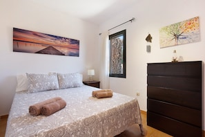 Un dormitorio con cama, almohadas, mesita de noche, ventana, puerta y decoración en la pared.