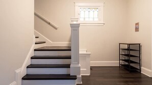 Un escalier avec des marches en bois foncé et des moulures blanches, menant à un palier doté d’une balustrade blanche et d’une fenêtre ornée de vitraux.