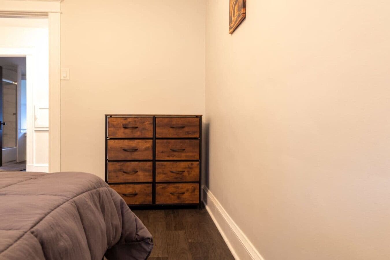 Un dormitorio con una cama, un aparador de madera y una puerta que da a otra habitación.